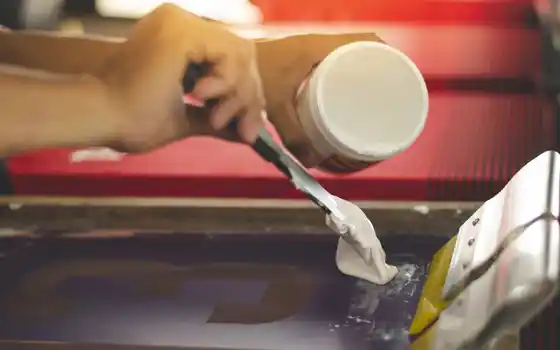 Auftragen von Siebdruckfarbe mit Spachtel auf einen Siebdruckrahmen während des Druckprozesses.