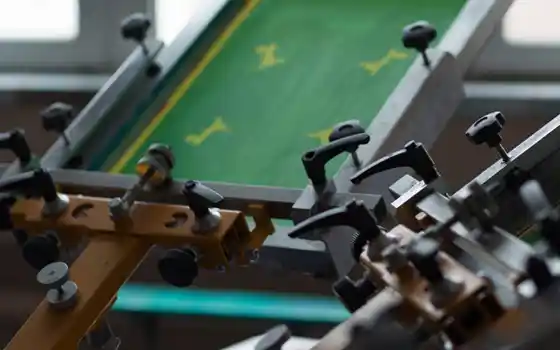 Siebdruckkarussell mit eingespanntem Siebdruckrahmen und mechanischen Halterungen.